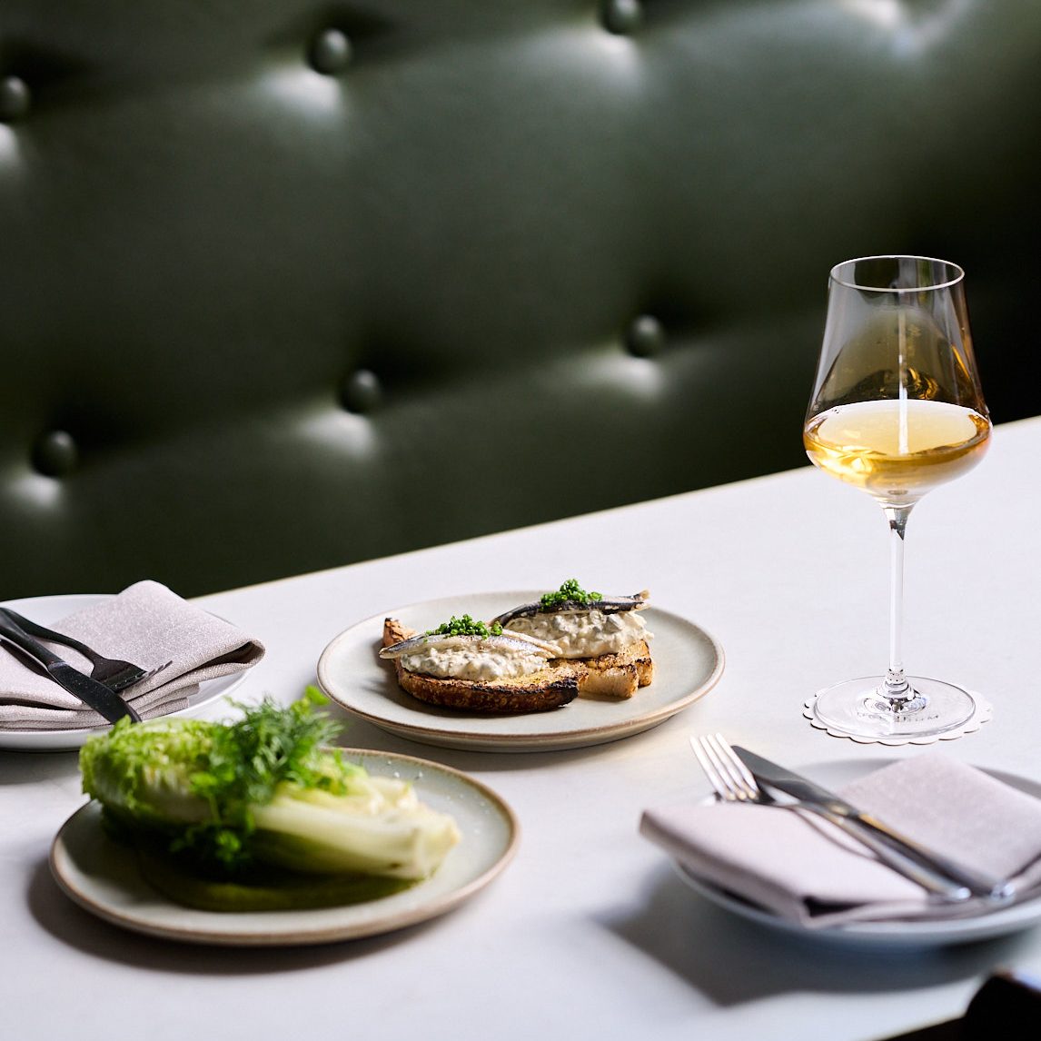 A beautifully set table with food, wine and a leather banquette in the background.