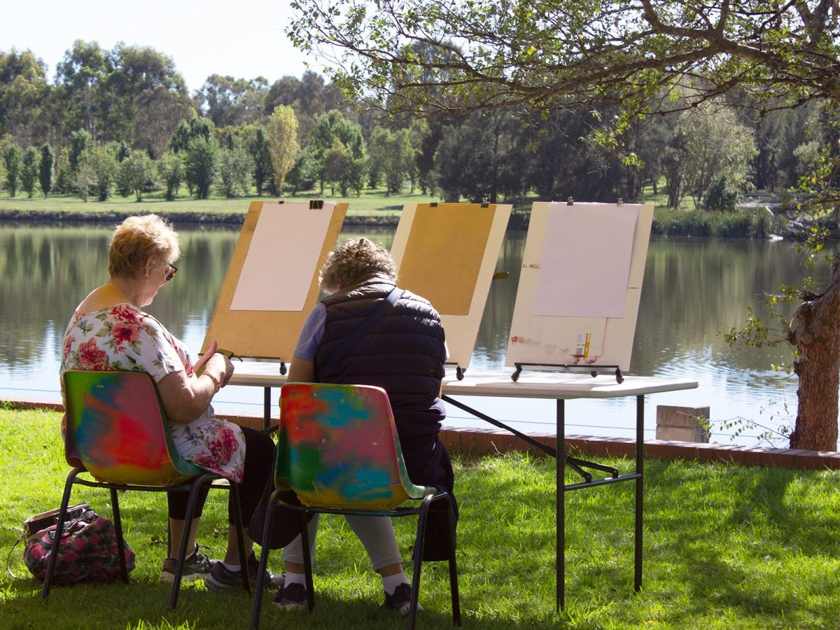 two people sitting in front of painting easels by the lake