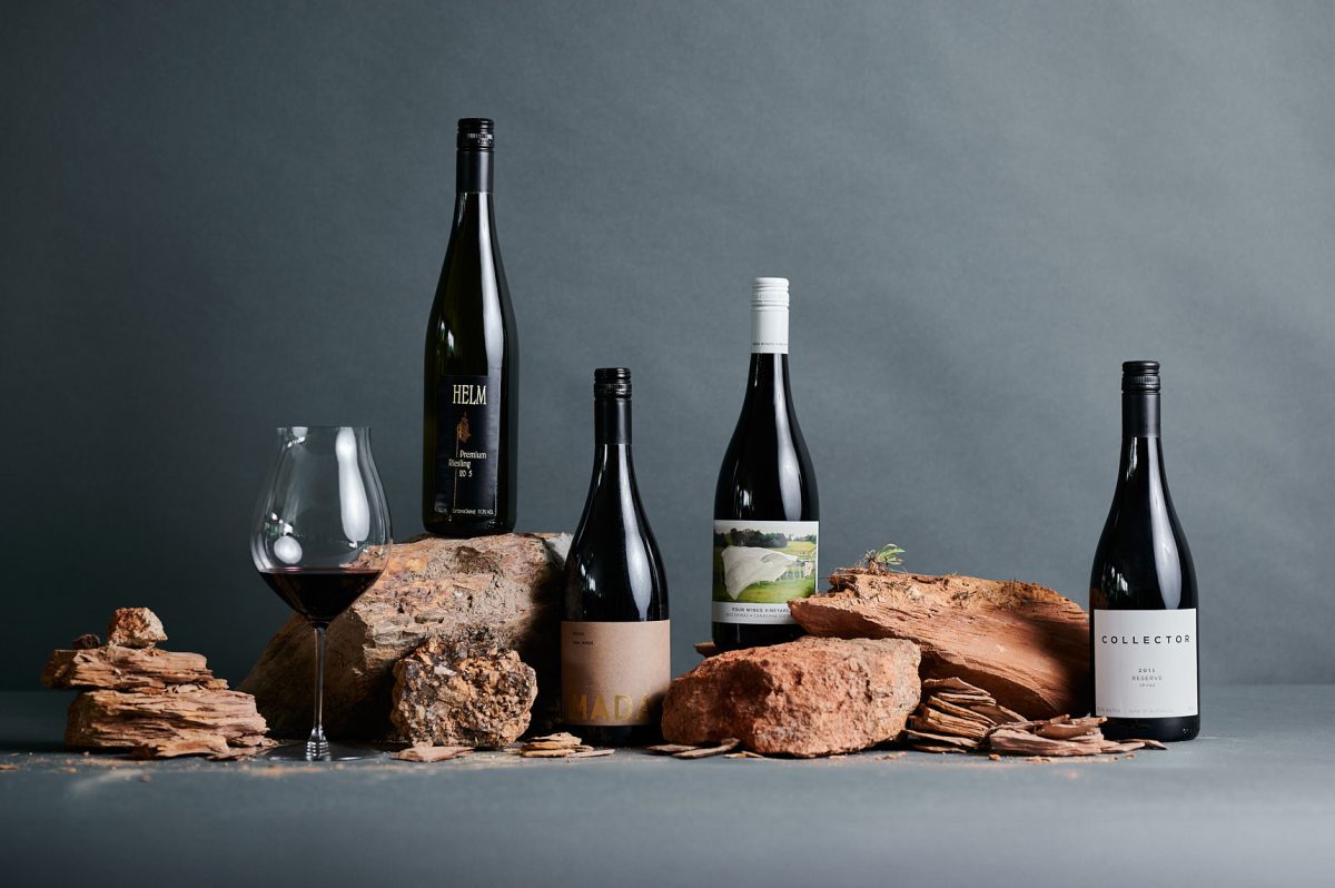 A styled shot of four bottles and one glass of wine against a grey background with different rocks. 