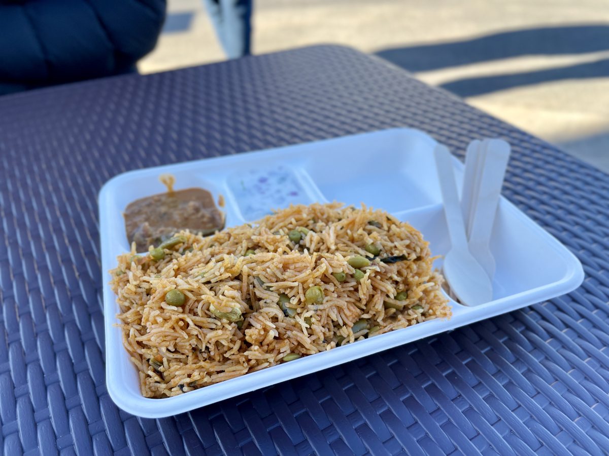 A cardboard tray with a heap of vegetables and rice, a chutney and raita.