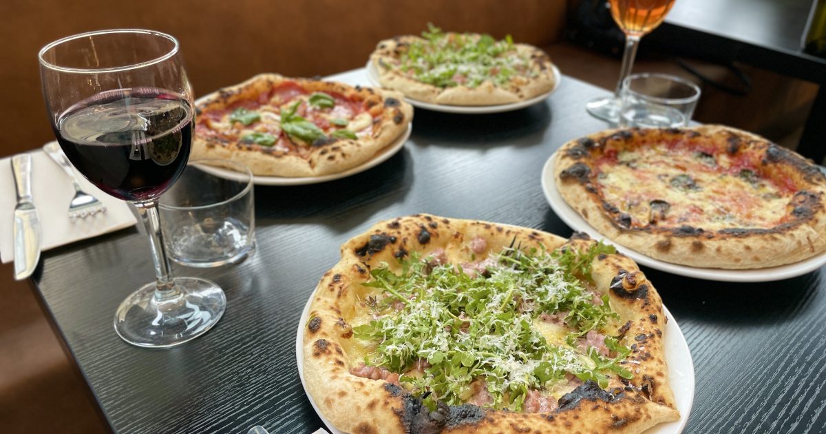 Four pizzas on a black restaurant table with two glasses of wine.