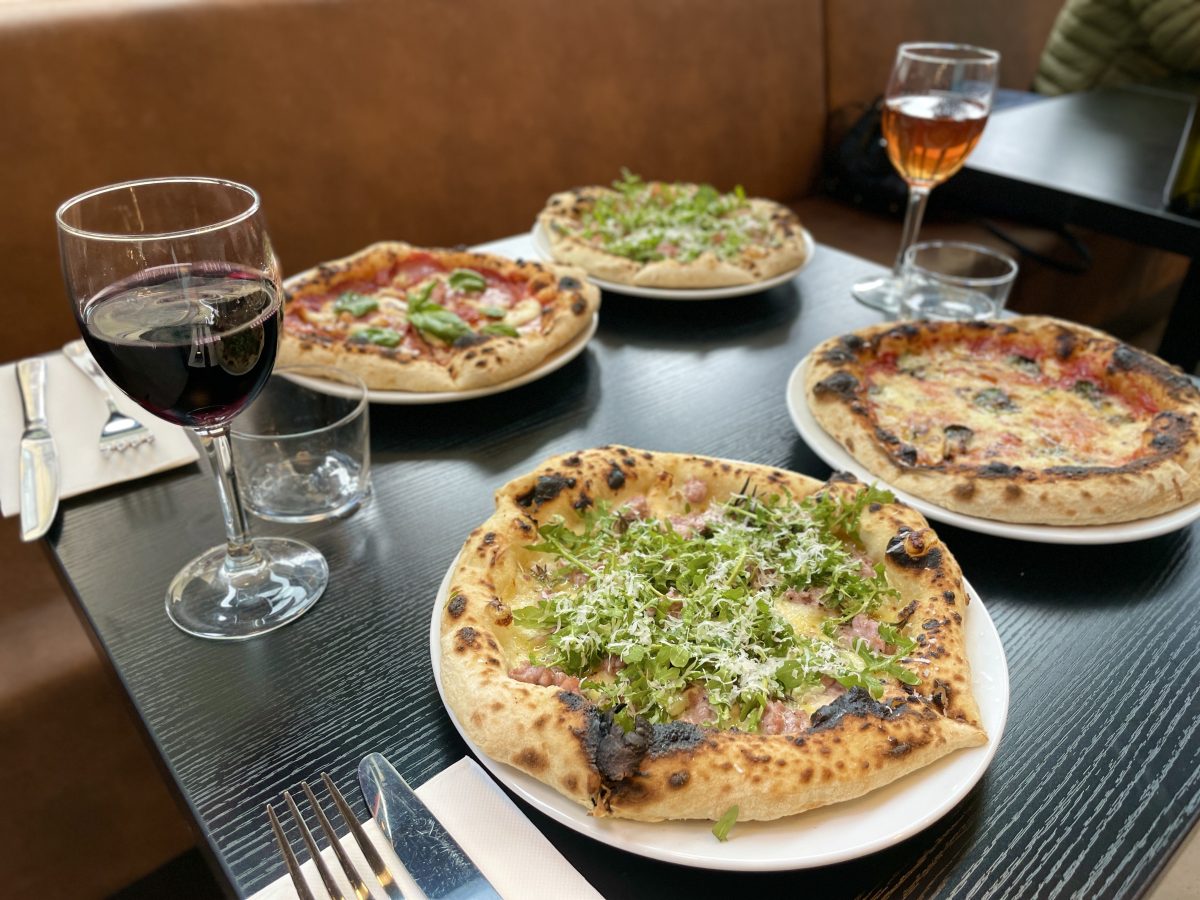 Four pizzas on a black restaurant table with two glasses of wine.