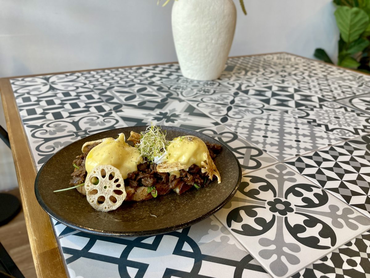 A plate with poached eggs under hollandaise sauce on top of beef with lotus chip garnish.