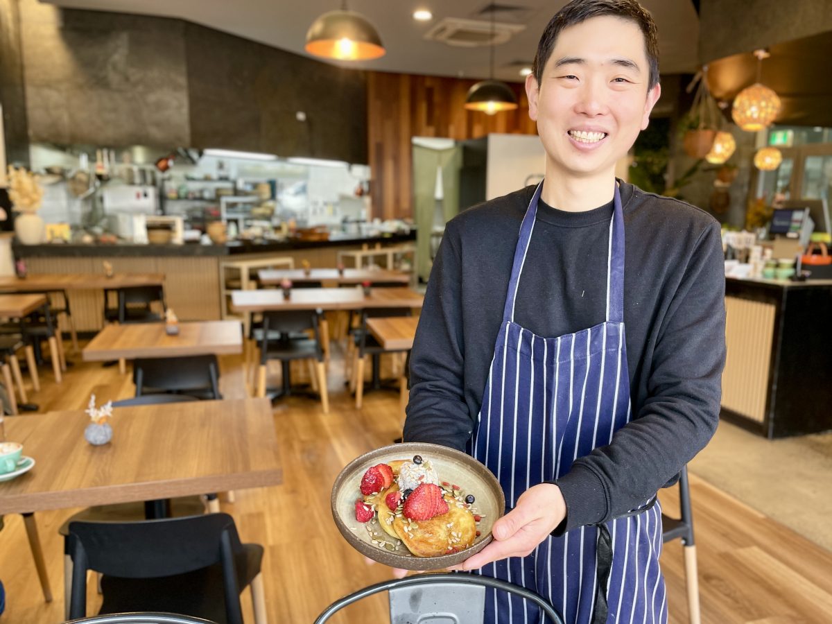 A chef holds a plate of pancakes topped with berries and ice cream in a cafe.