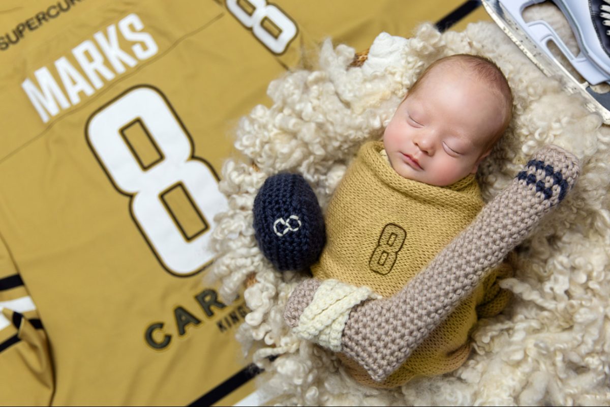 Baby on a hockey jersey with a crocheted hockey stick