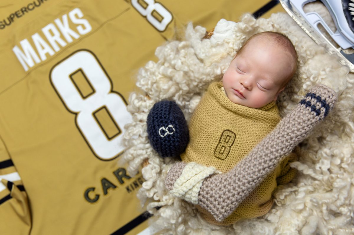 Baby on a hockey jersey with a crocheted hockey stick