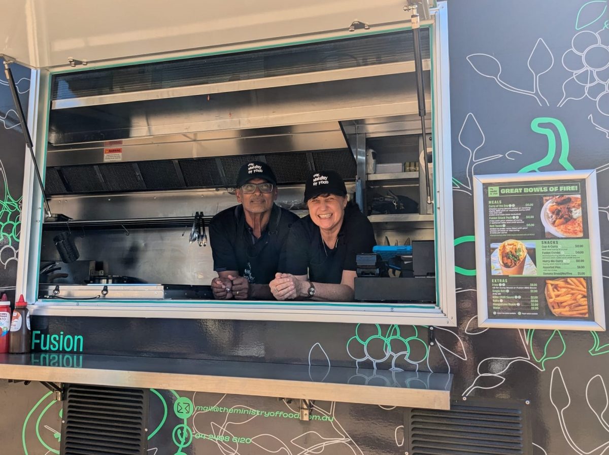Two people smile behind the counter of a food truck