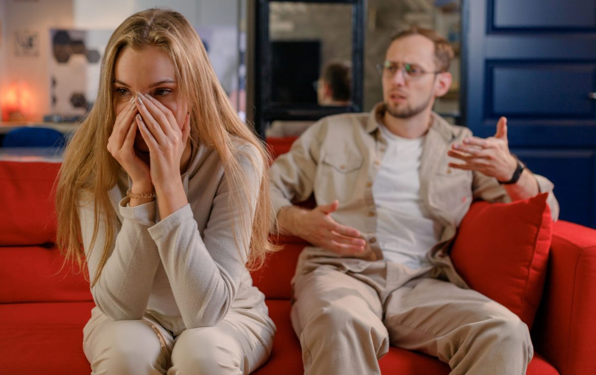 woman looking stressed on couch while man argues with her