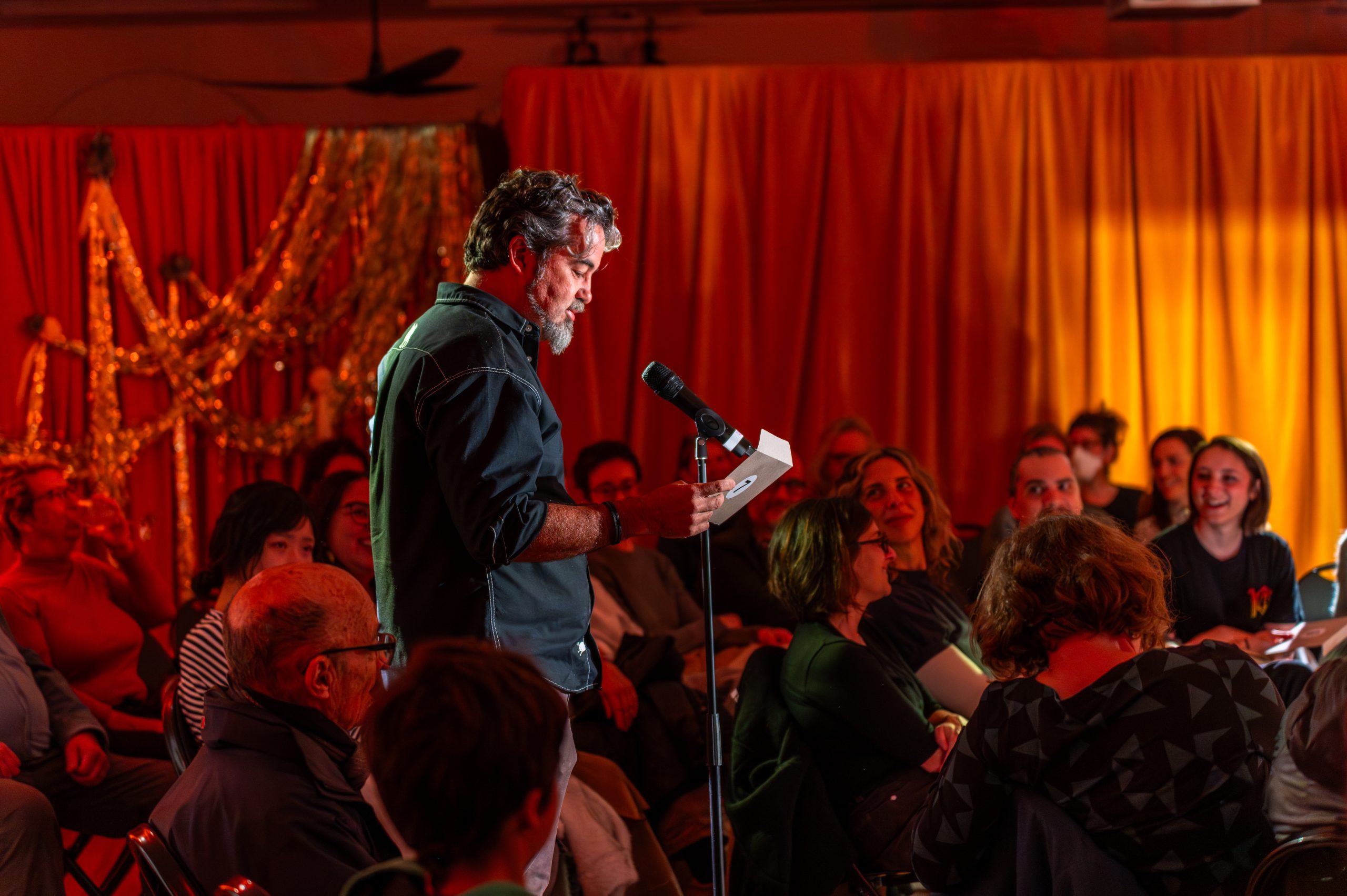 a person reading from a piece of paper speaking into a microphone in front of a crowd of people sitting down