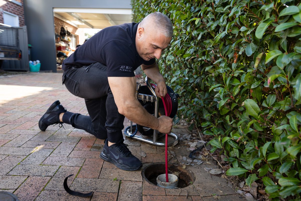 a man kneeling on the ground next to a drain, using equipment to unblock the drain