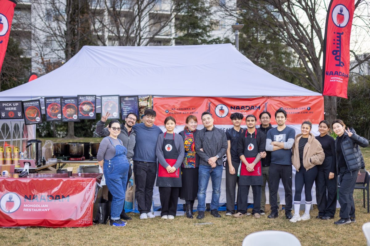 A group photo outside a tent branded with Naadam logo.