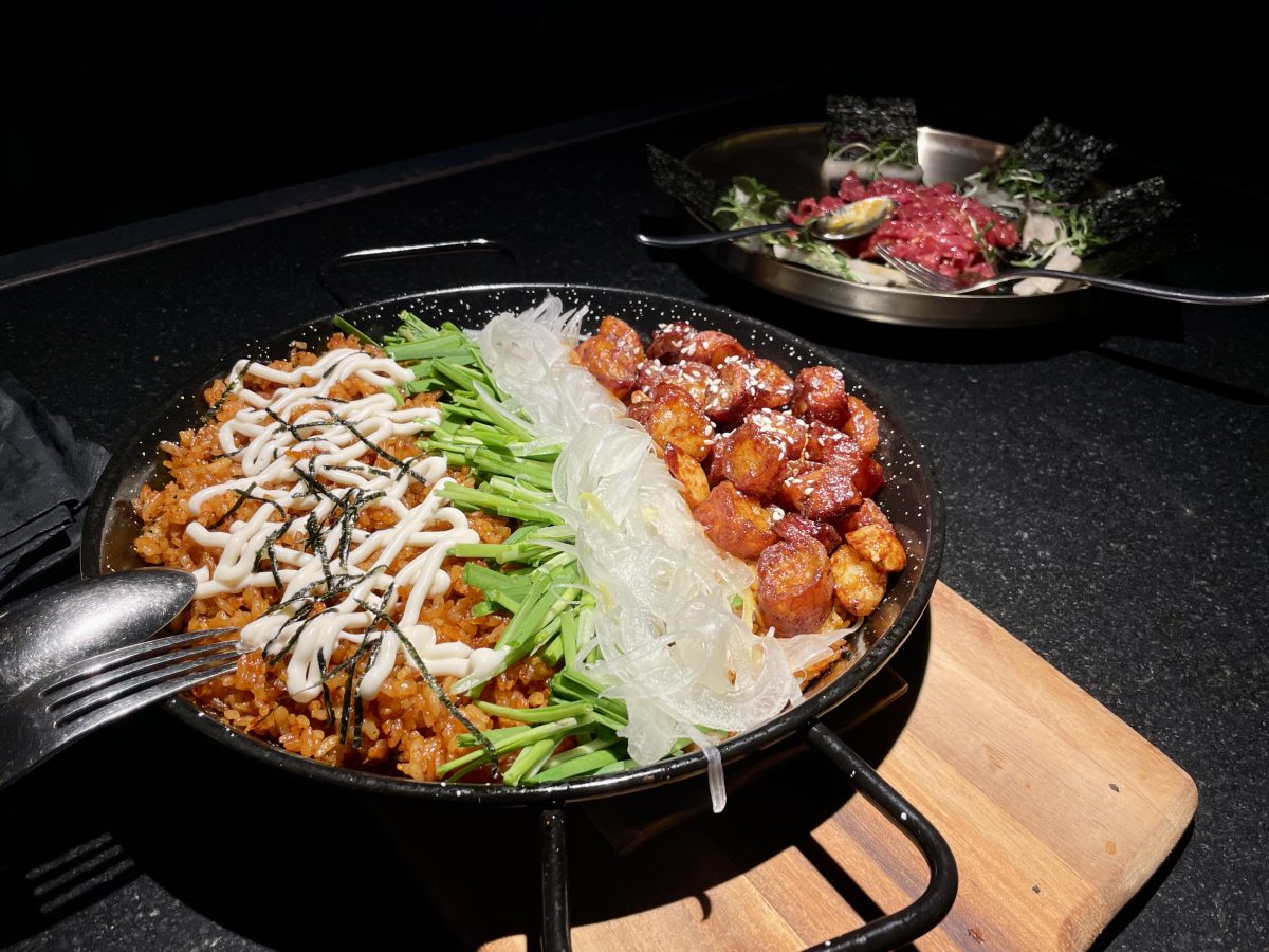 A wide, shallow pan of fried rice, in the background a dish with raw beef.