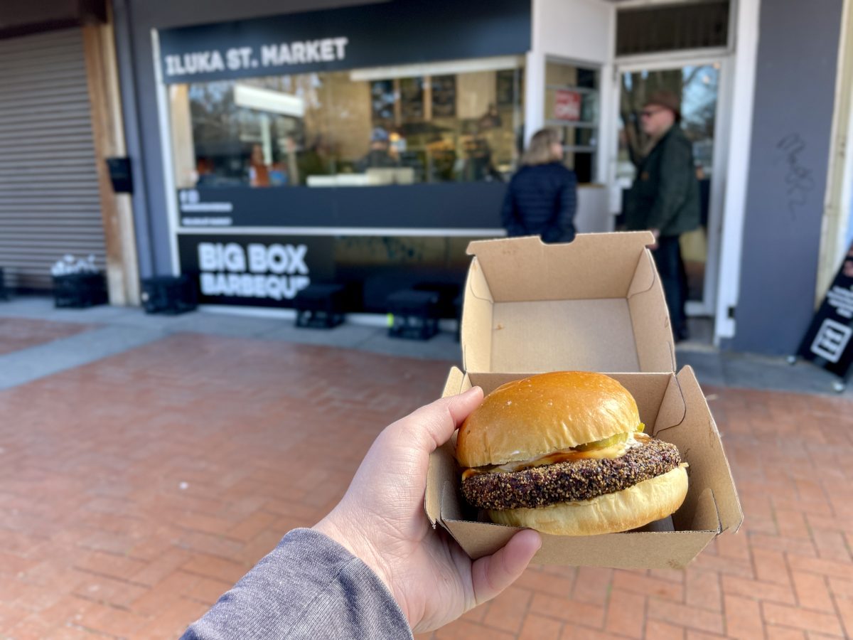 A cardboard takeaway box with a burger inside, in the background is Big Box Barbecue signage.