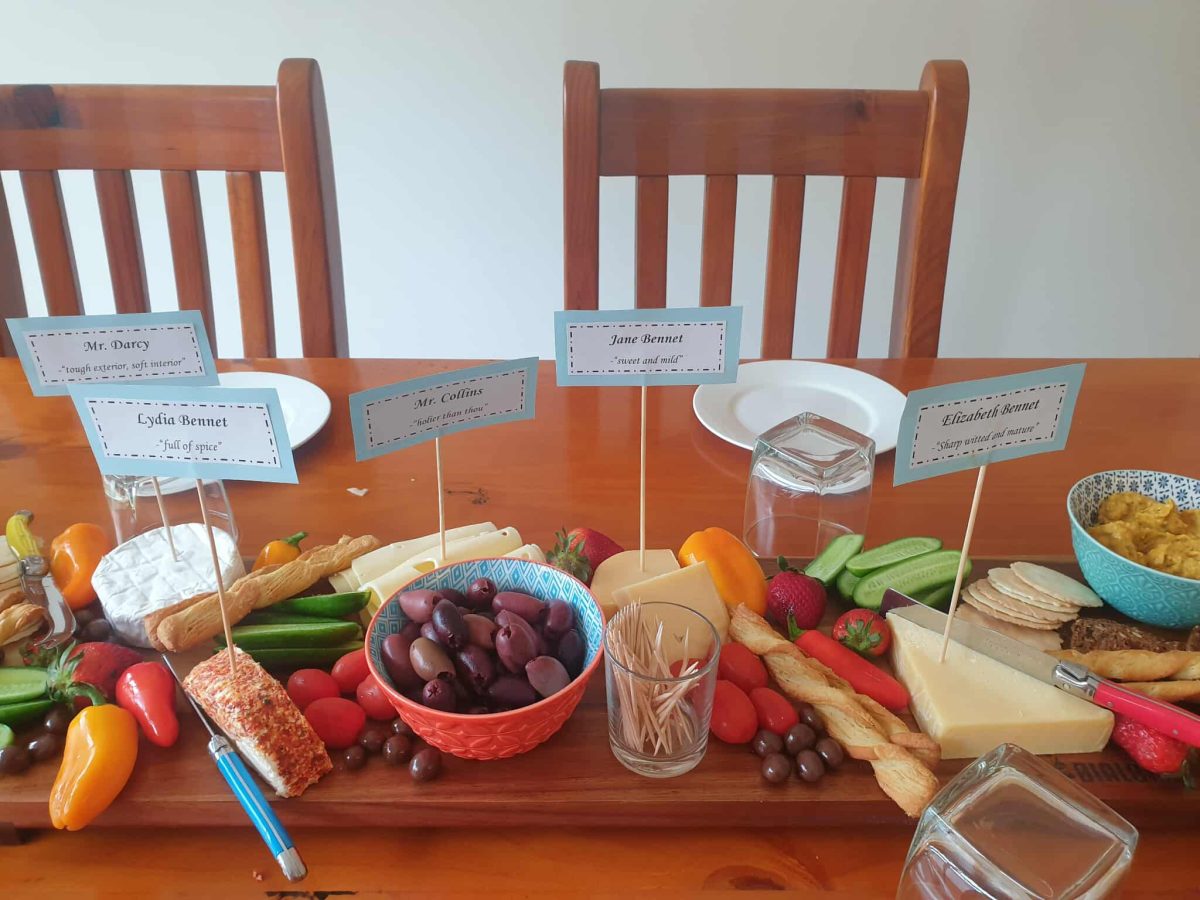 A dining table set with a selection of grazing snacks. Each cheese has a label with names based on characters from Pride & Prejudice.