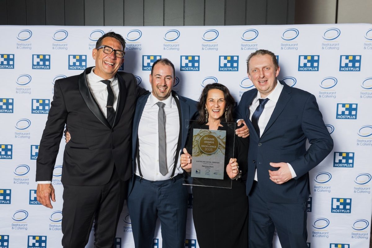 A group photo of four people: three men in suits and one woman holding a prize.