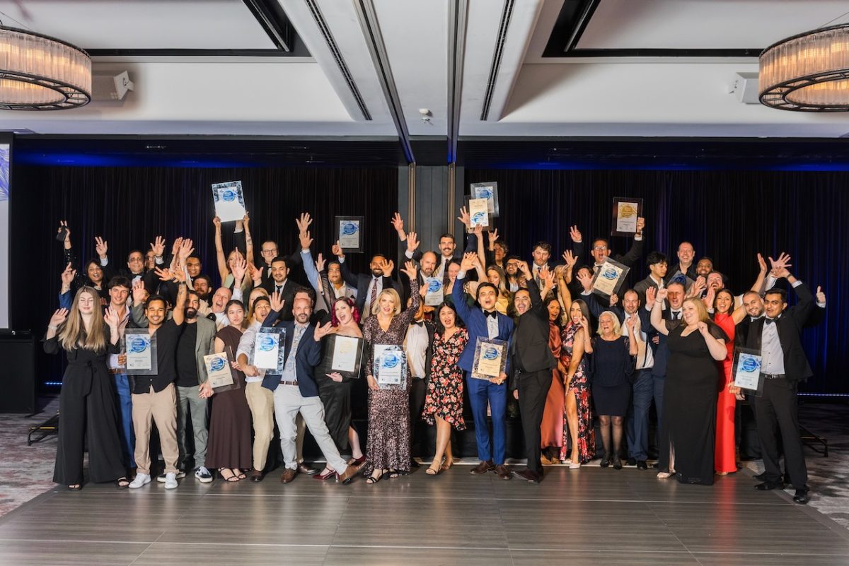 A large group photo of winners in black tie holding up their awards.