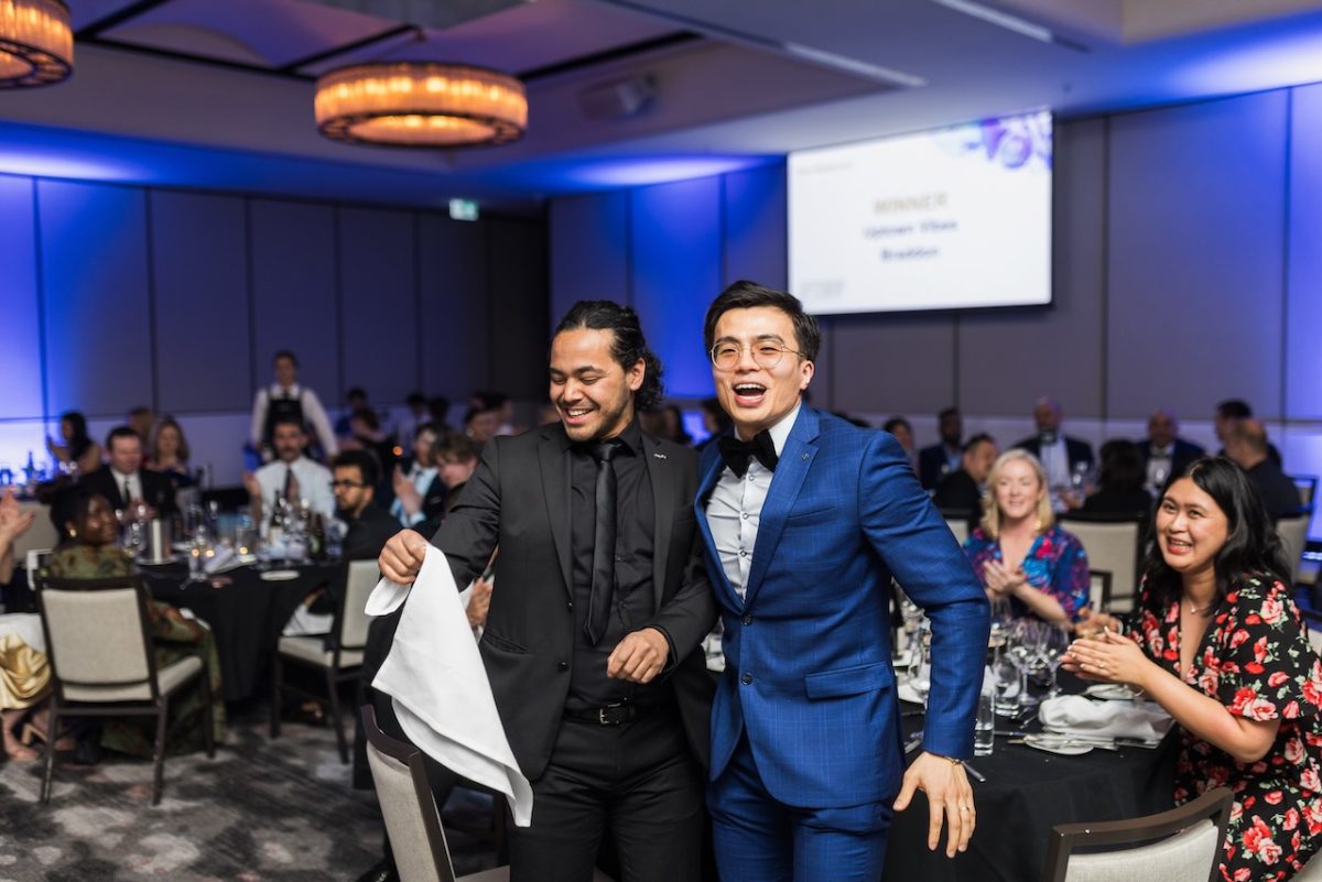 Two men in suits getting up from their table look excited about winning an award.