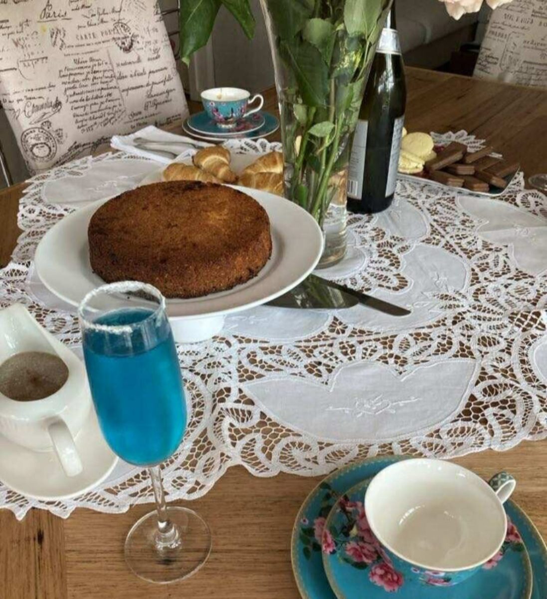 A sophisticated table set ornately with a cream doily, tea cake and flower painted tea set.