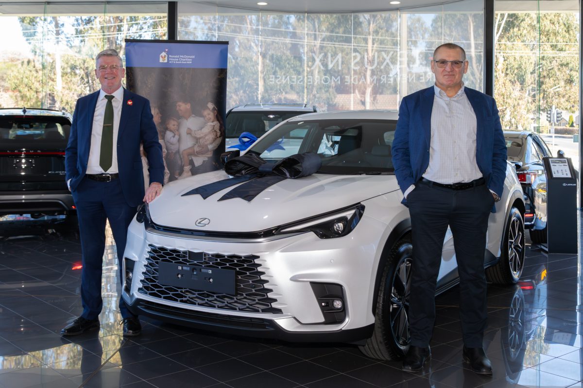 Ronald McDonald House Canberra CEO Eoghan O'Byrne with local businessman Mirko Milic of Lexus of Canberra standing by a new car in a car dealership.