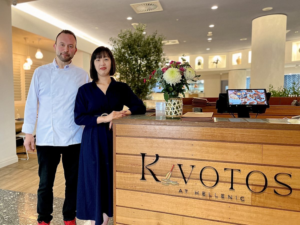 A man in chefs whites standing next to a woman in blue dress at the front counter of Kivotos.