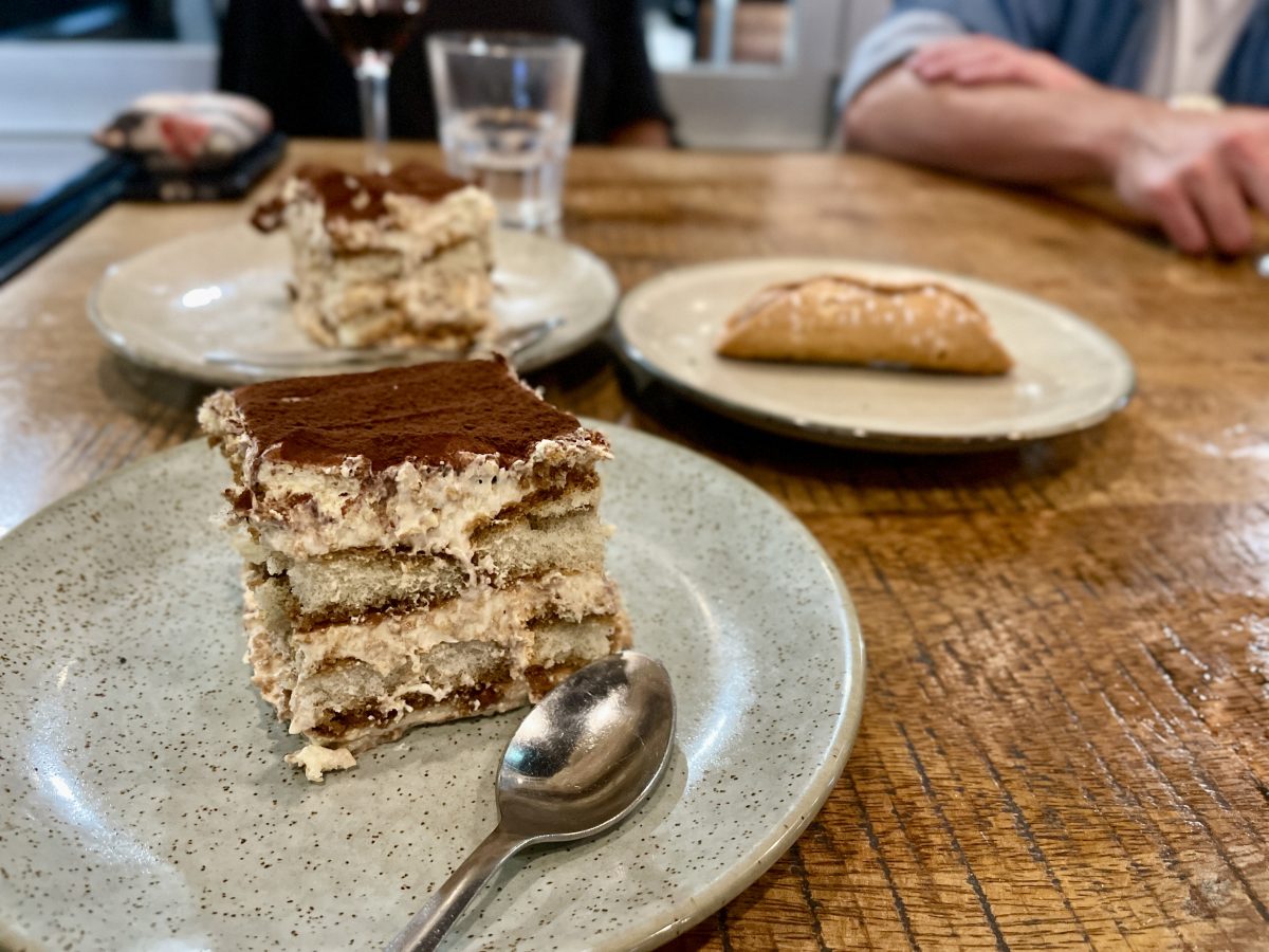 A slab of tiramisu with a cannoli in the background