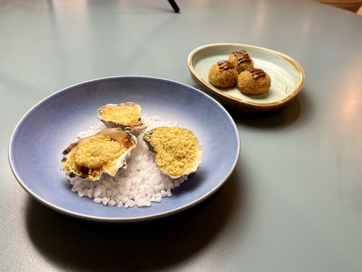 A plate of baked oysters, with arancini balls behind.