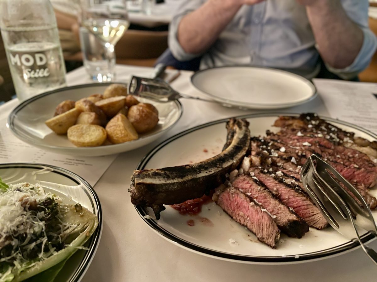 Plate of sliced rib-eye steak, a bowl of potatoes and a salad in the foreground.