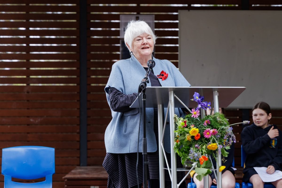 Stephanie Alexander, an older white woman, stands at a podium decorated with flowers.