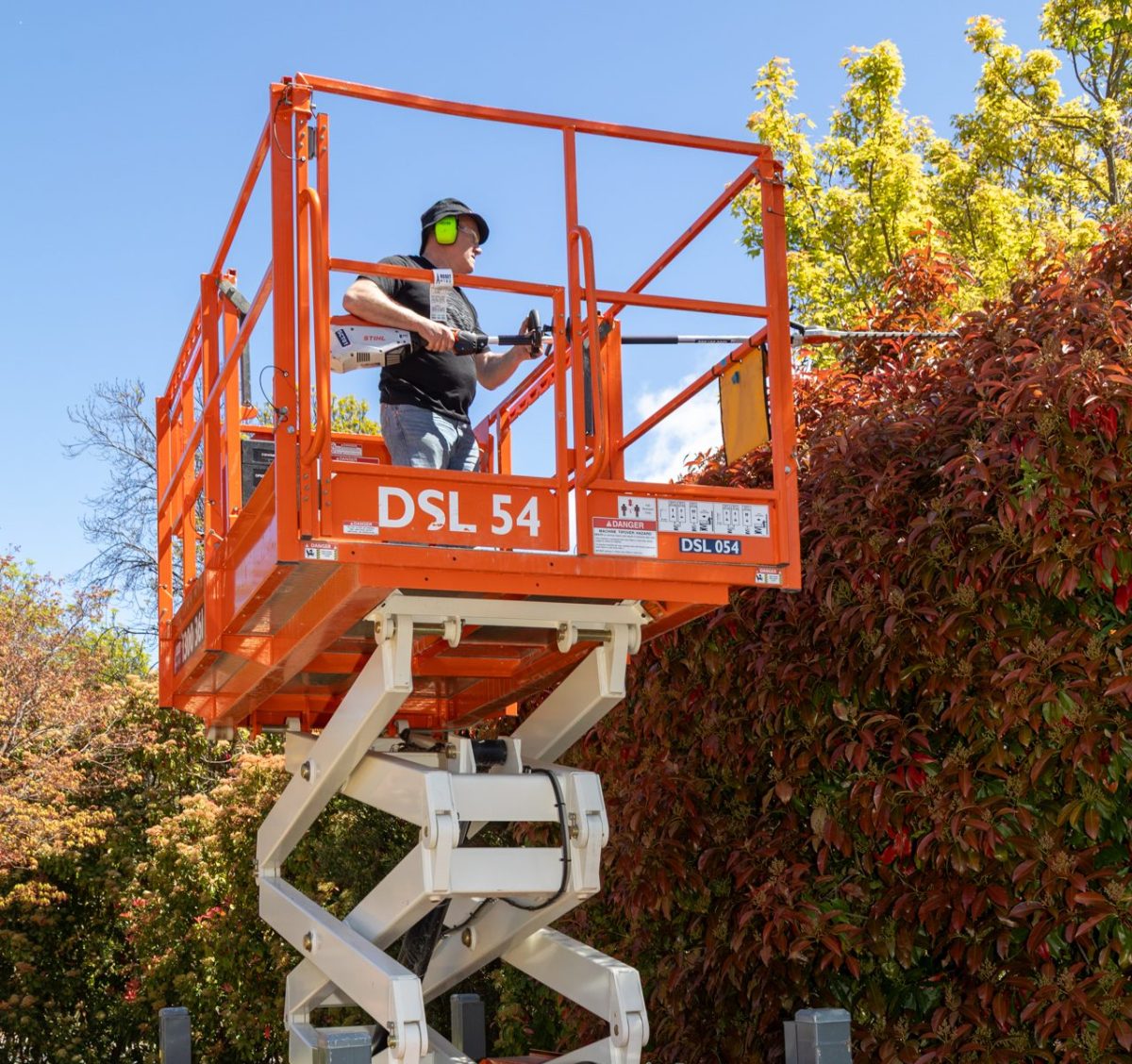 man on scissor lift trimming a hedge