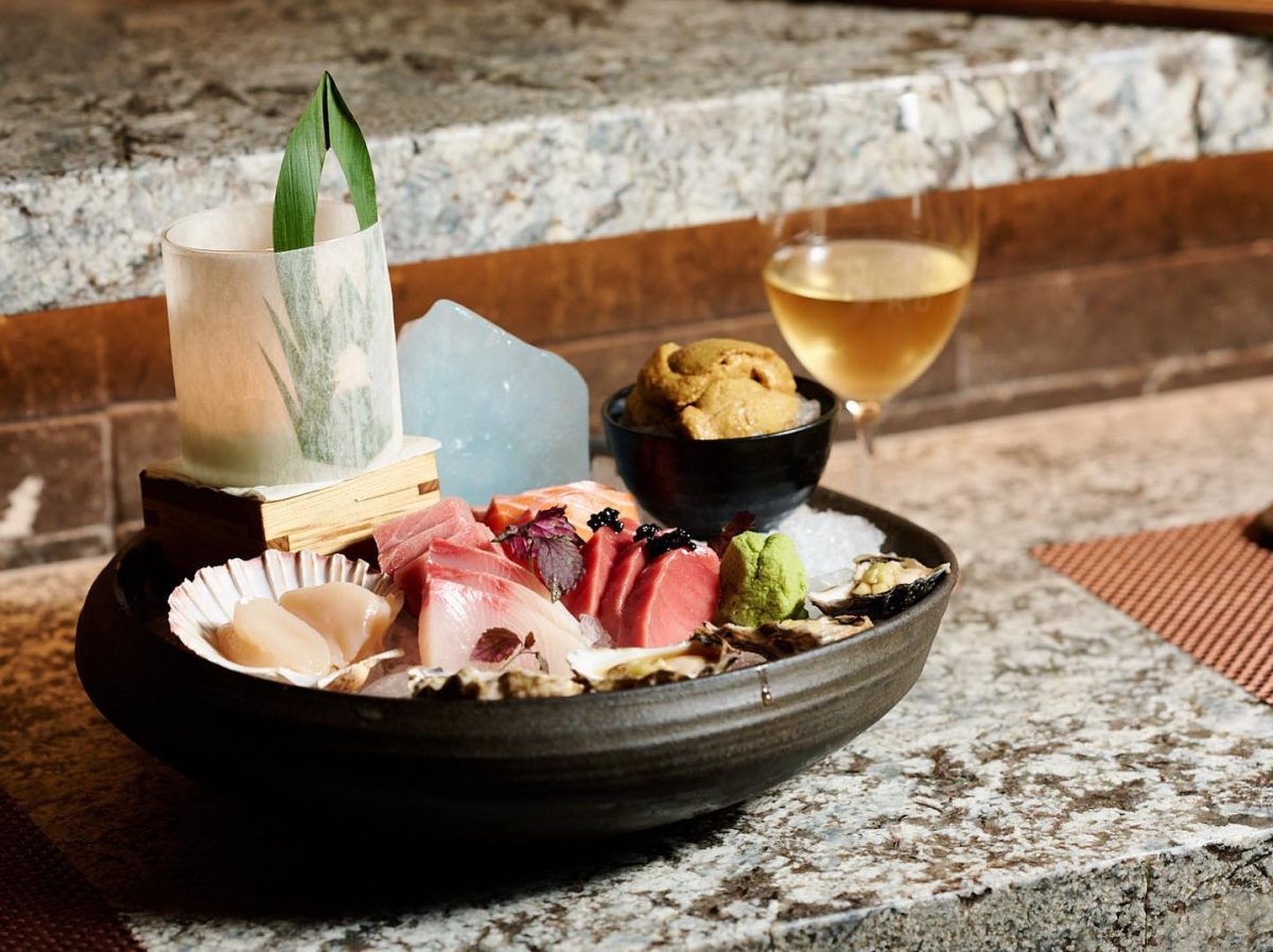 An impressive plate of sashimi, including a bowl of sea urchin roe, with a glass of wine.