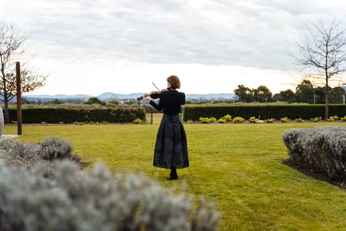 Woman plays violin in field.