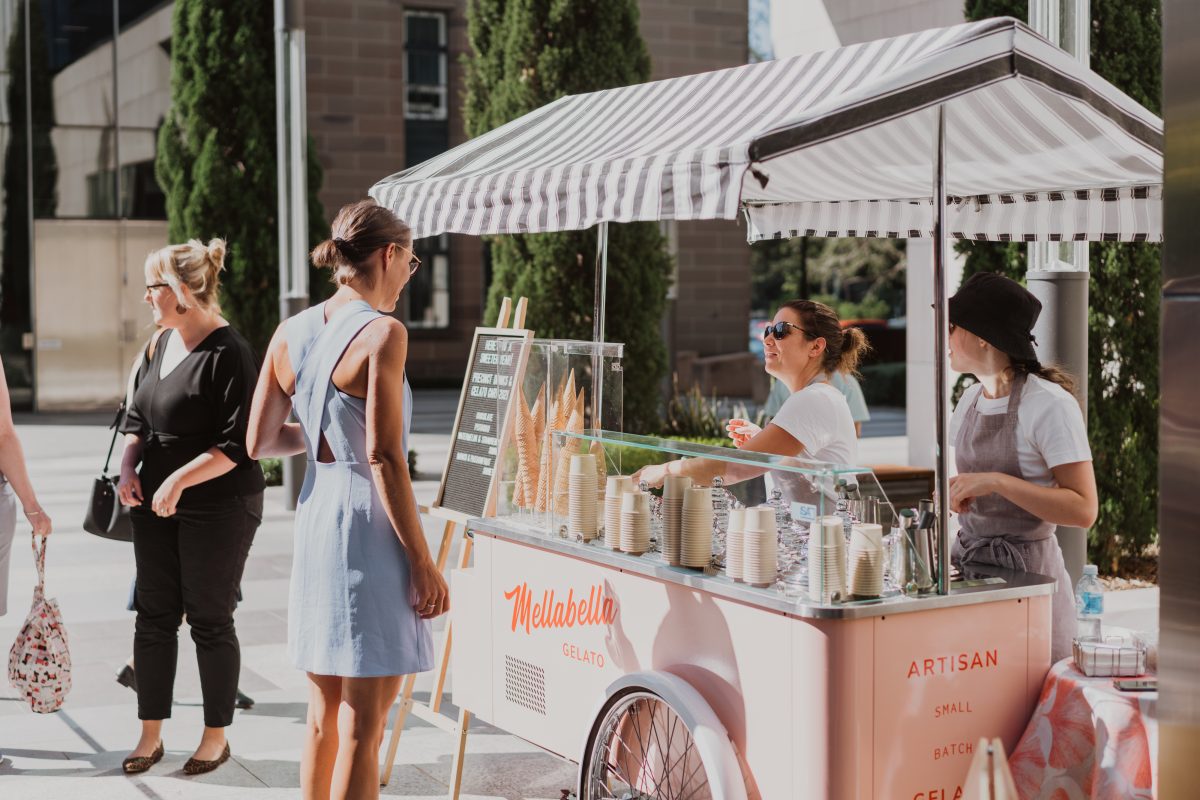 A pink gelato cart with striped awning serving gelato at an event.
