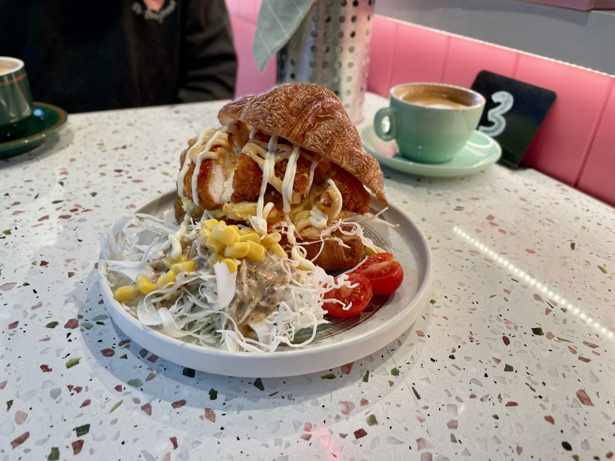 A croissant filled with scrambled egg and chicken katsu, a small cabbage salad on the side. 