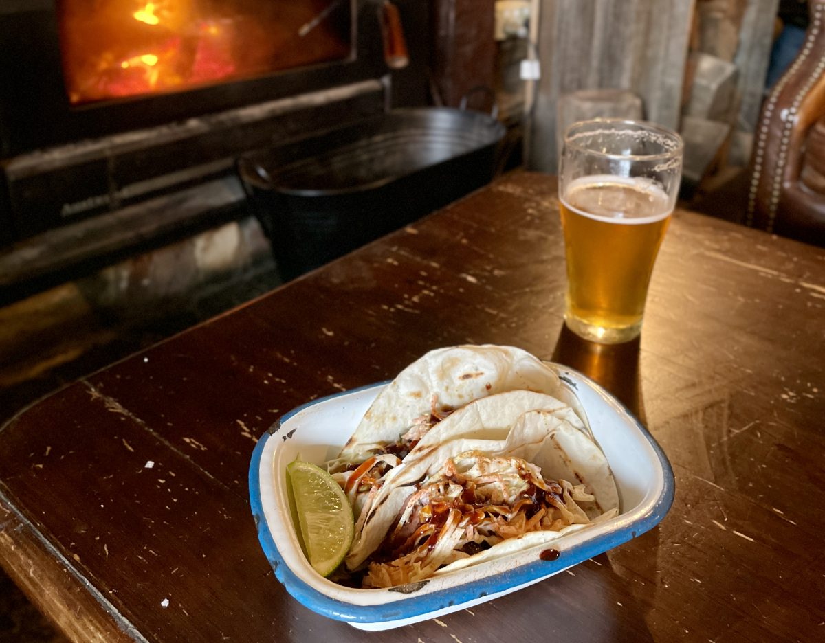 Tacos on a table with beer in front of a fire.