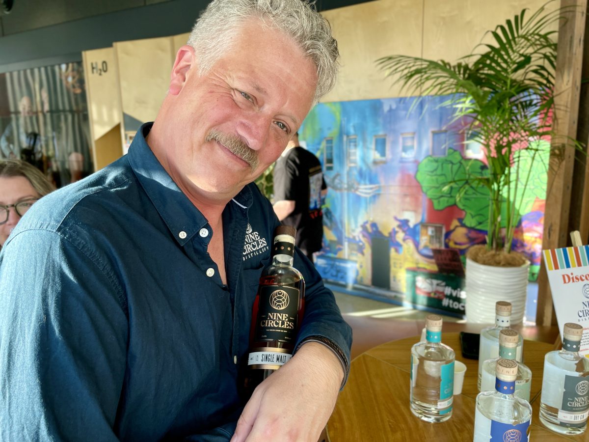 A man with a moustache jokingly cradles a bottle of Nine Circles whisky in his arms.