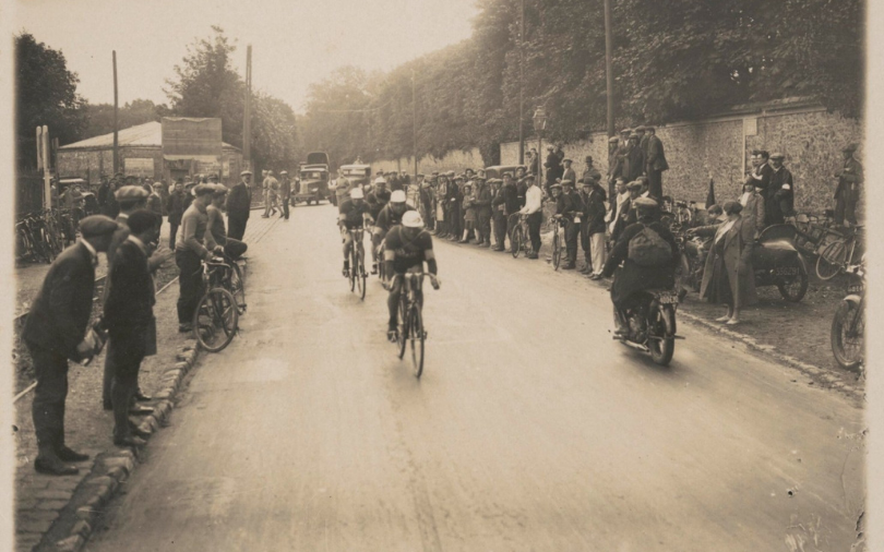 Cyclists riding through a village while the street is lined by spectators