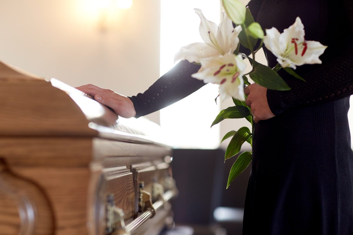 Woman with lillies puts her hand on a casket