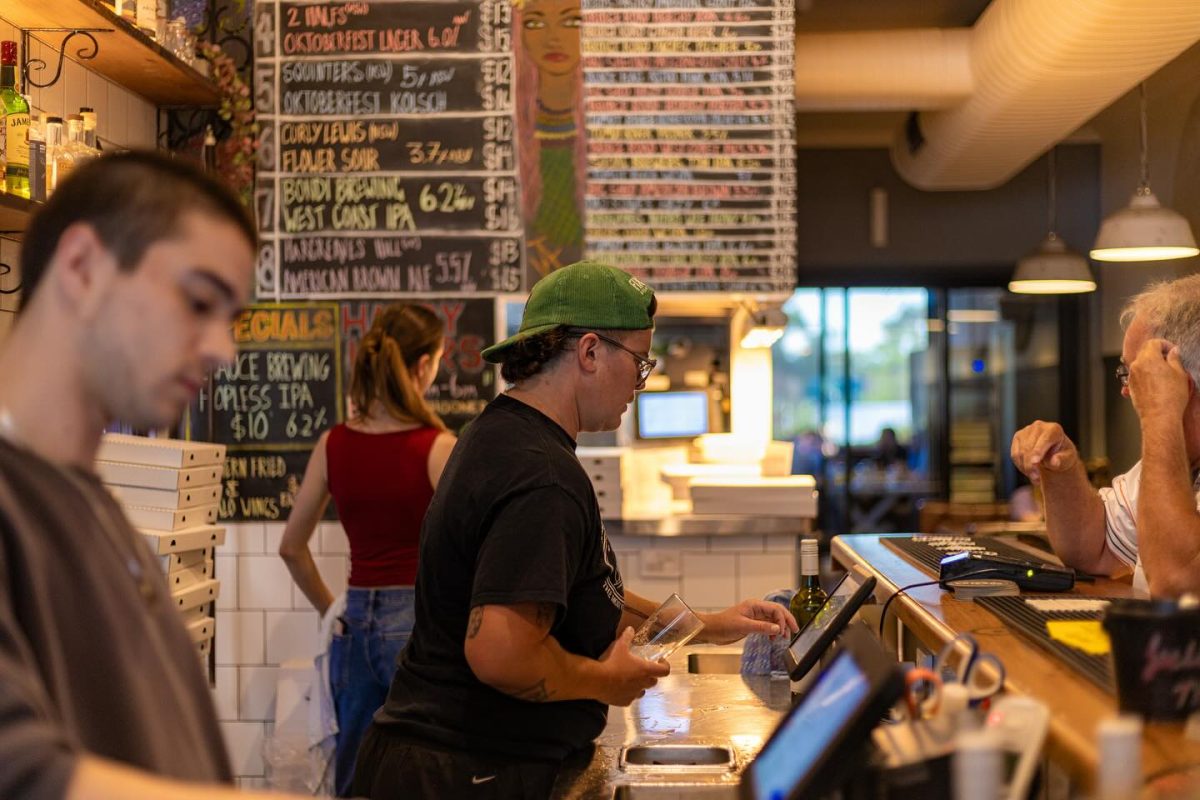 A woman with backwards cap serves customers at a bar.