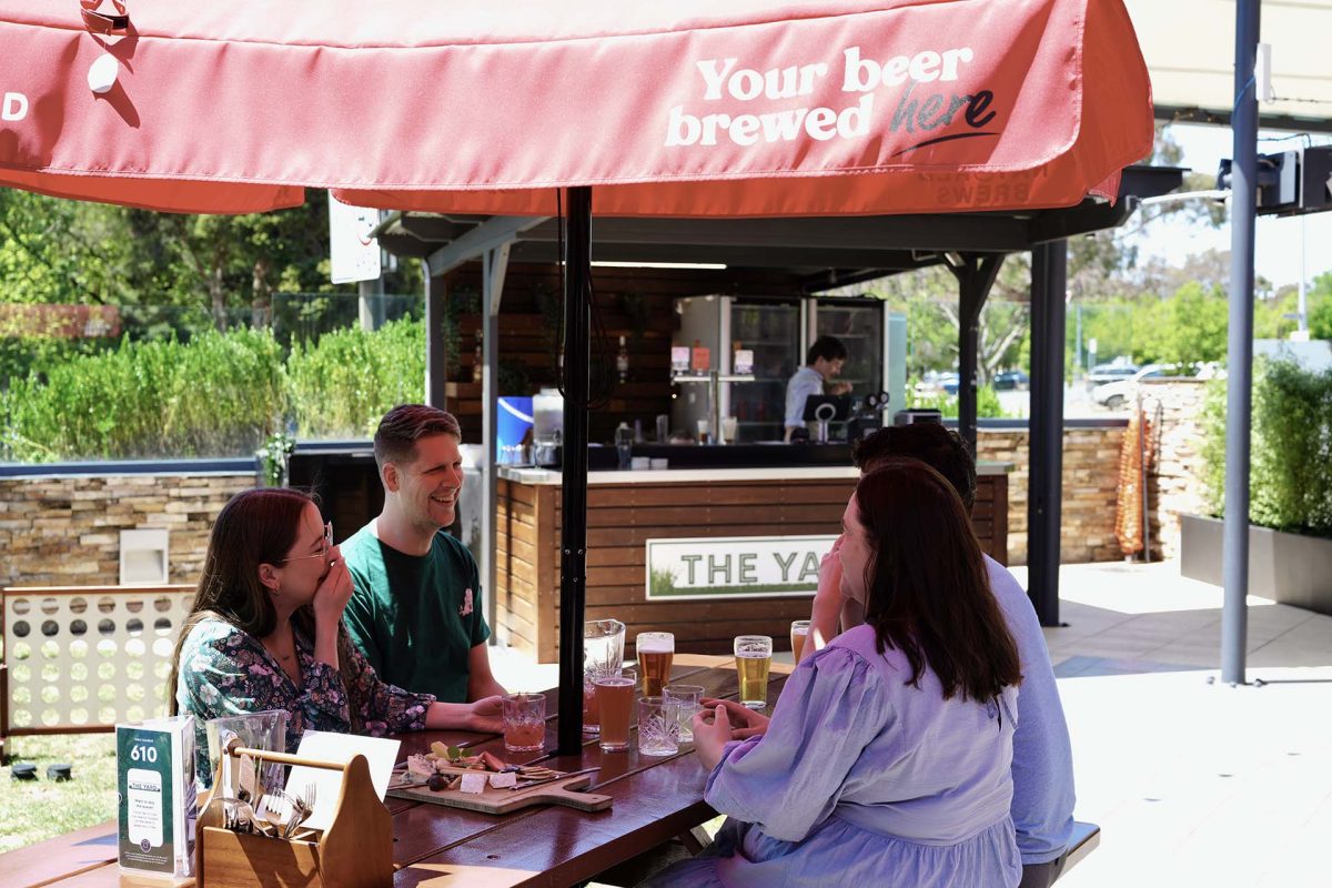 people sitting on a table outdoors under an umbrella