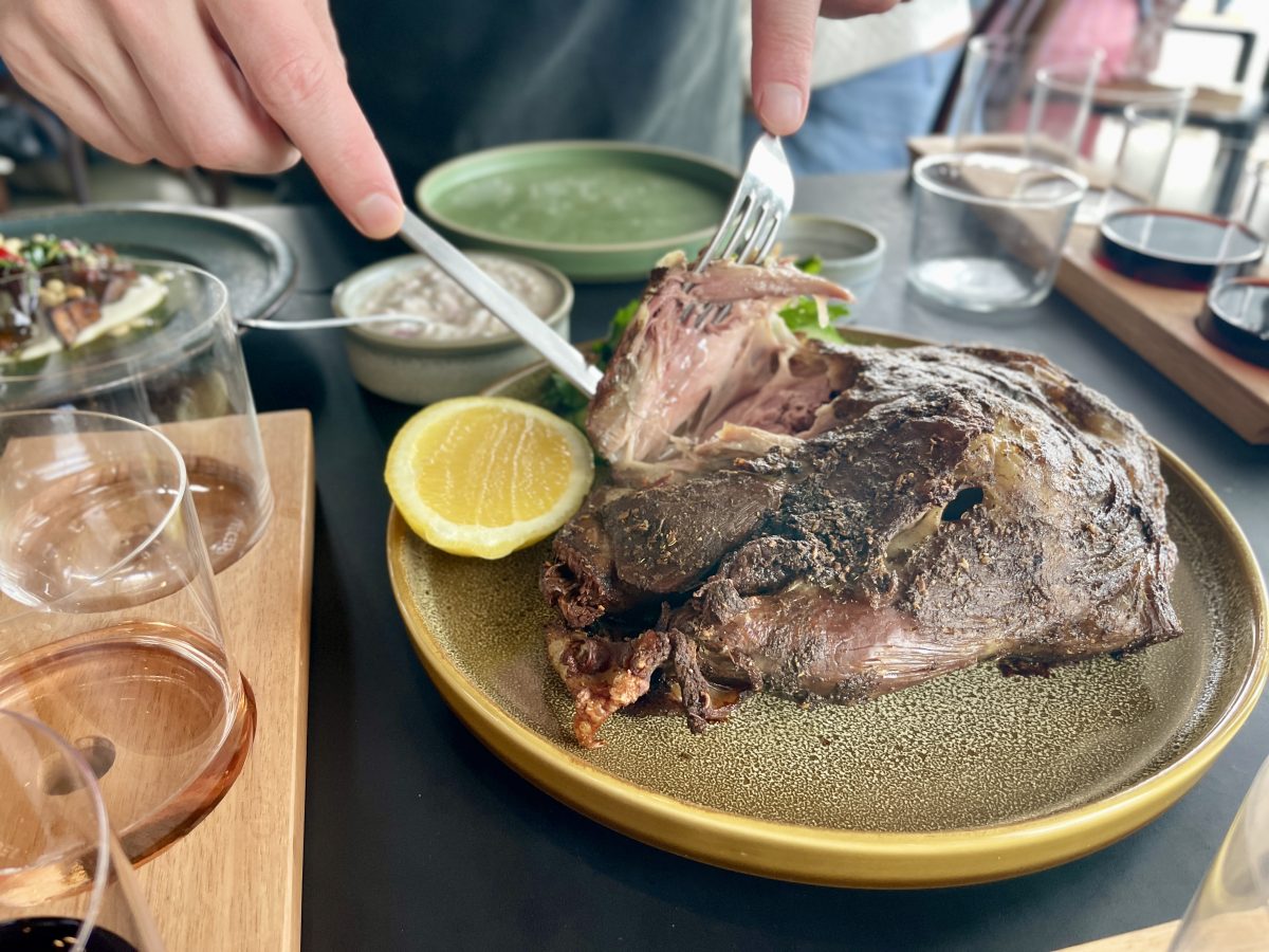 A hand pulling tender meat off a lamb shoulder with a fork.