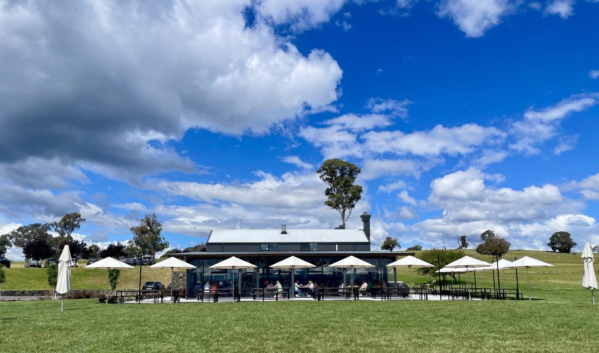 A building sitting behind a green lawn with umbrellas and a blue sky.