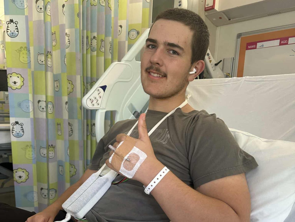 A teenager sitting in a hospital bed, giving a 'thumbs up' with one hand