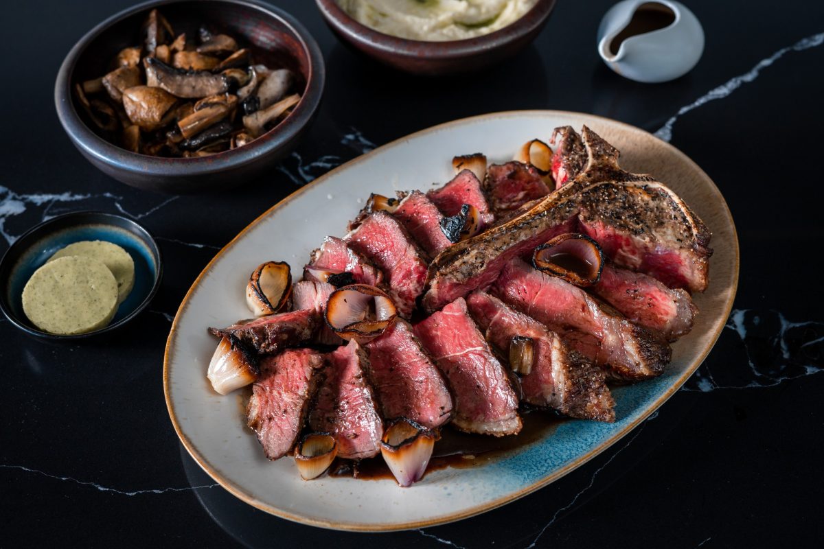 A tasty looking T-bone steak sliced to show a rare interior and topped with grilled onion medallion.