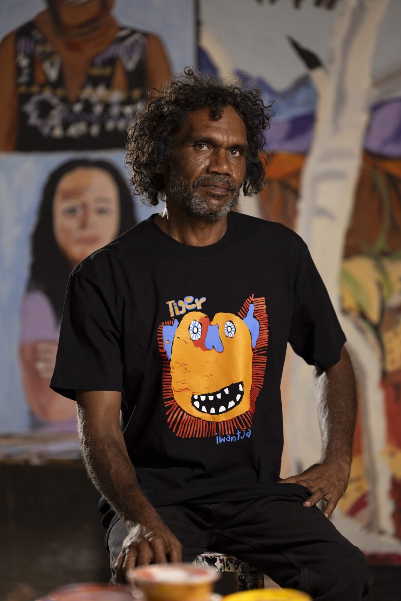 Photograph of an Aboriginal artist in front of his paintings