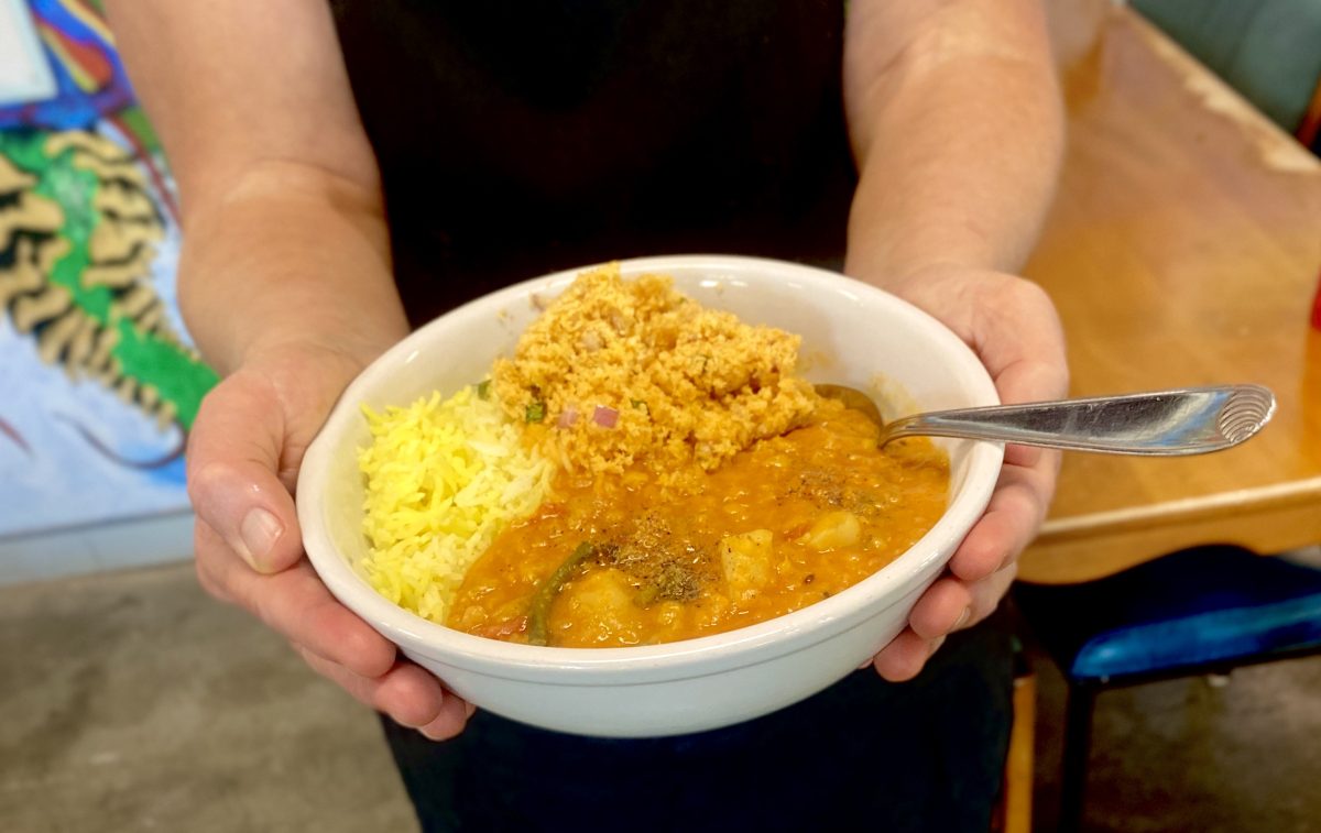 Hands holding a bowl of curry and rice. It looks hearty, wholesome and generous.