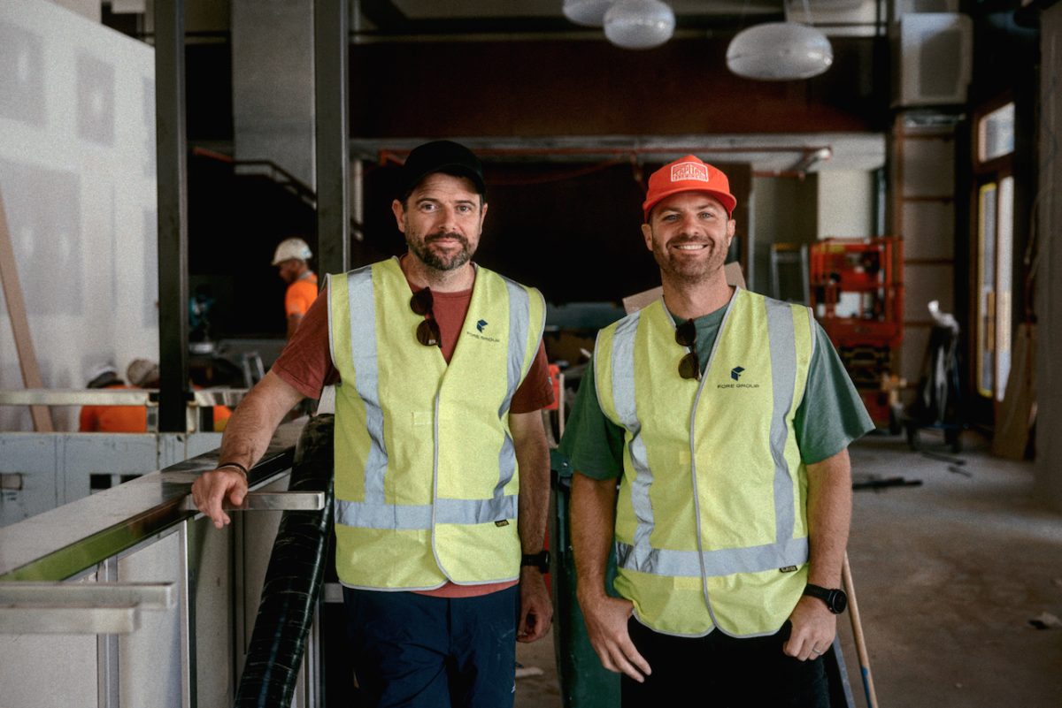 Two men in caps and yellow safety vests stand in a pub under construction.