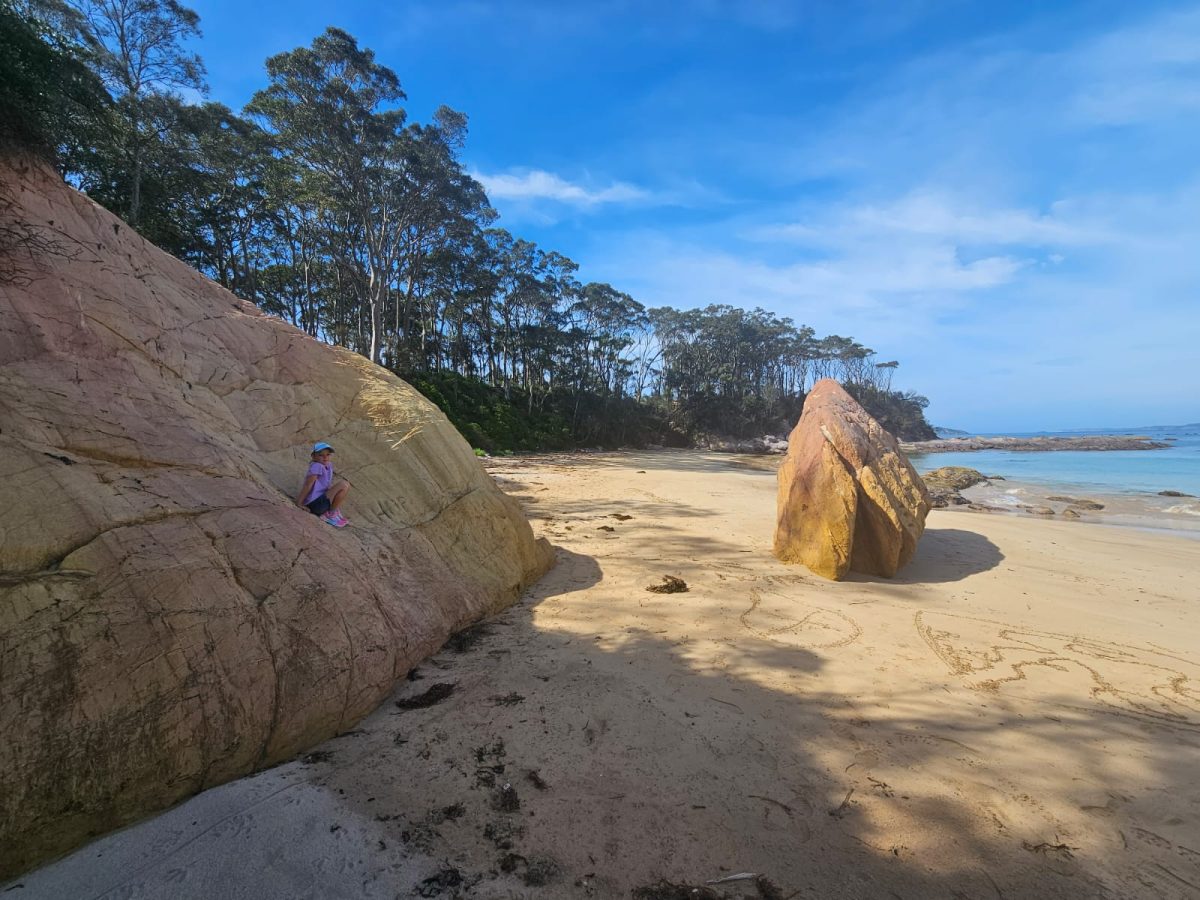 A large rock formation on the beach, with a small child perched midway up the rock, looking peaceful.