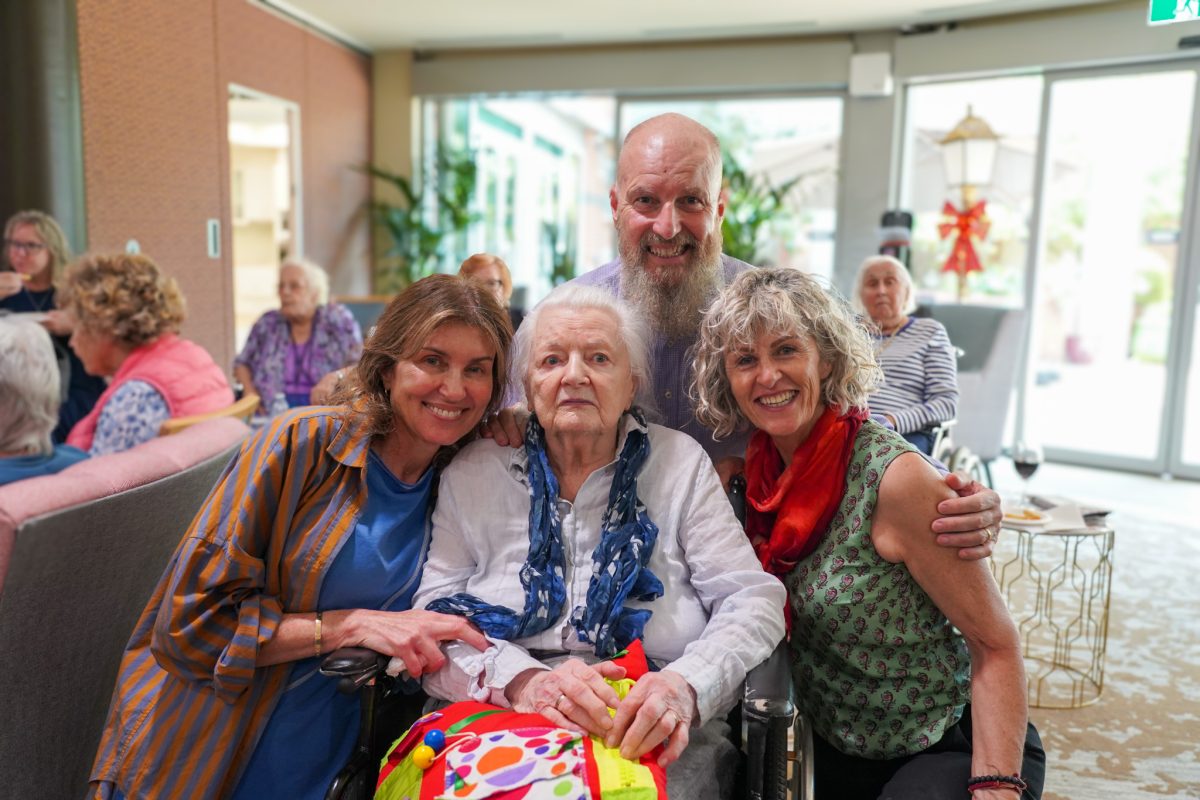 three people with an elderly woman in a wheelchair at an aged-care centre