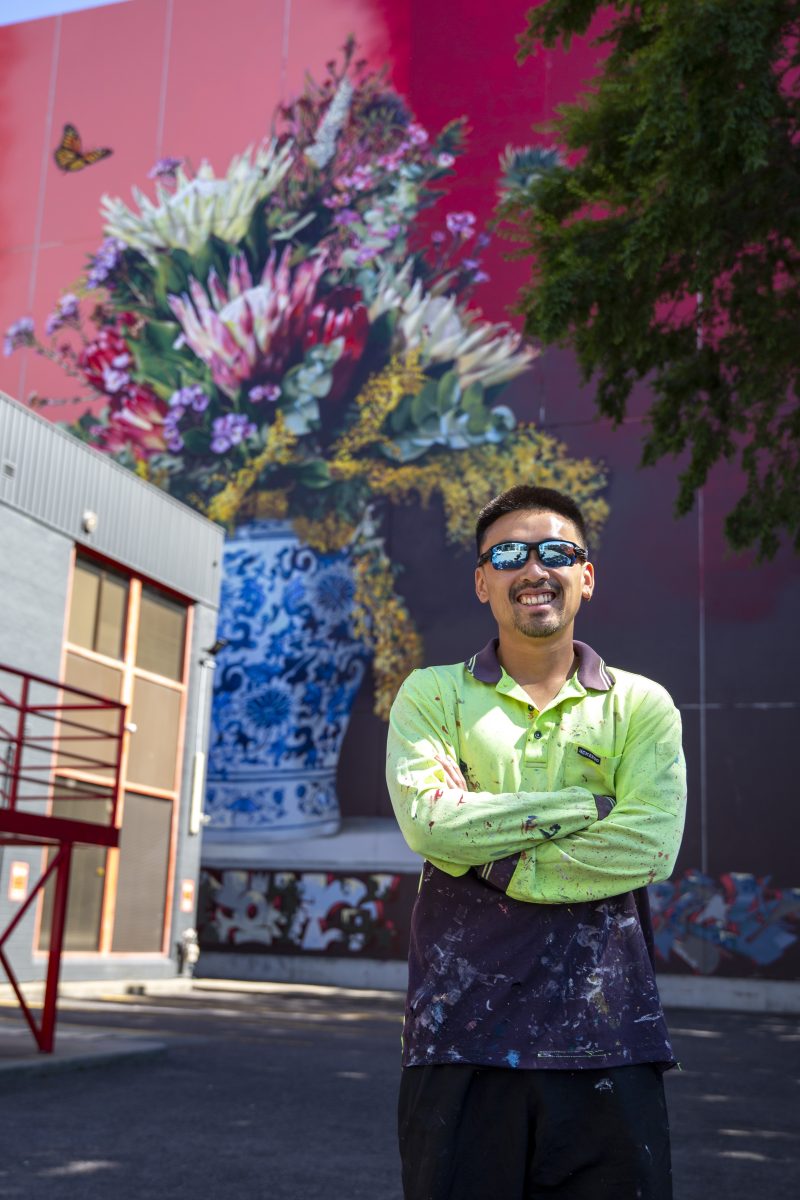 man standing in front of large-scale floral mural