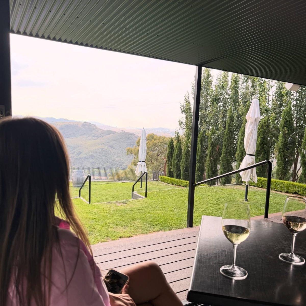 a person sitting on a deck with a glass of wine on the table looking at a view outside